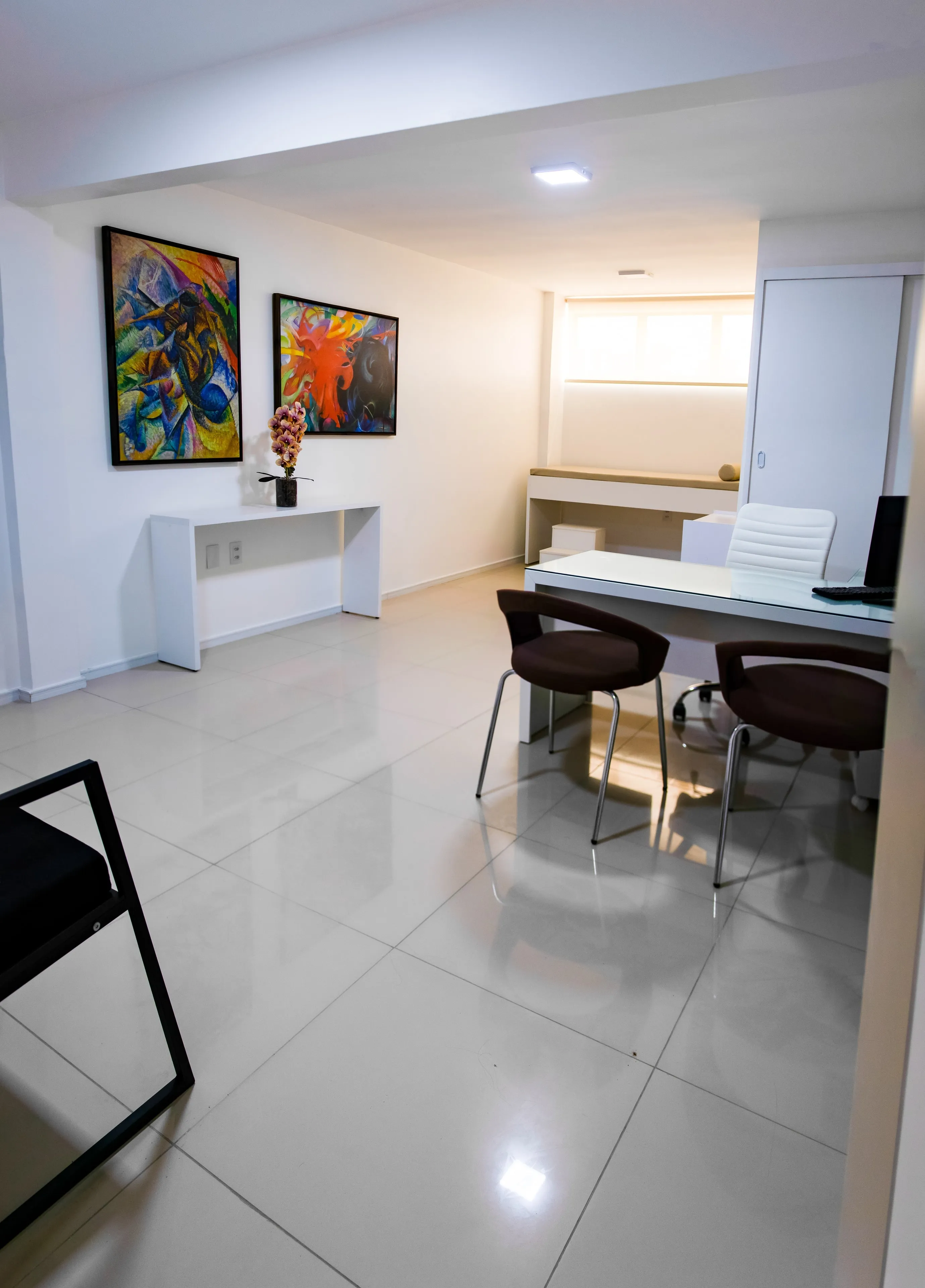 Consultório com mesa de atendimento, cadeiras e quadros coloridos nas paredes
