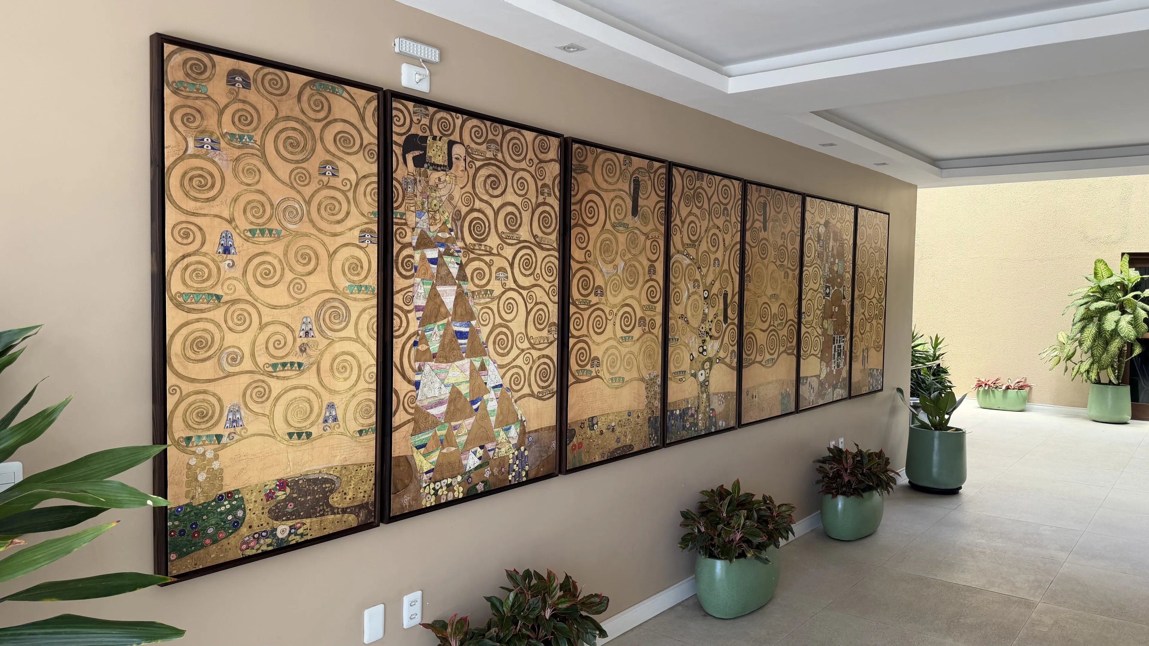 Pátio com painéis dourados inspirados na obra de Gustav Klimt, vasos com plantas e piso claro